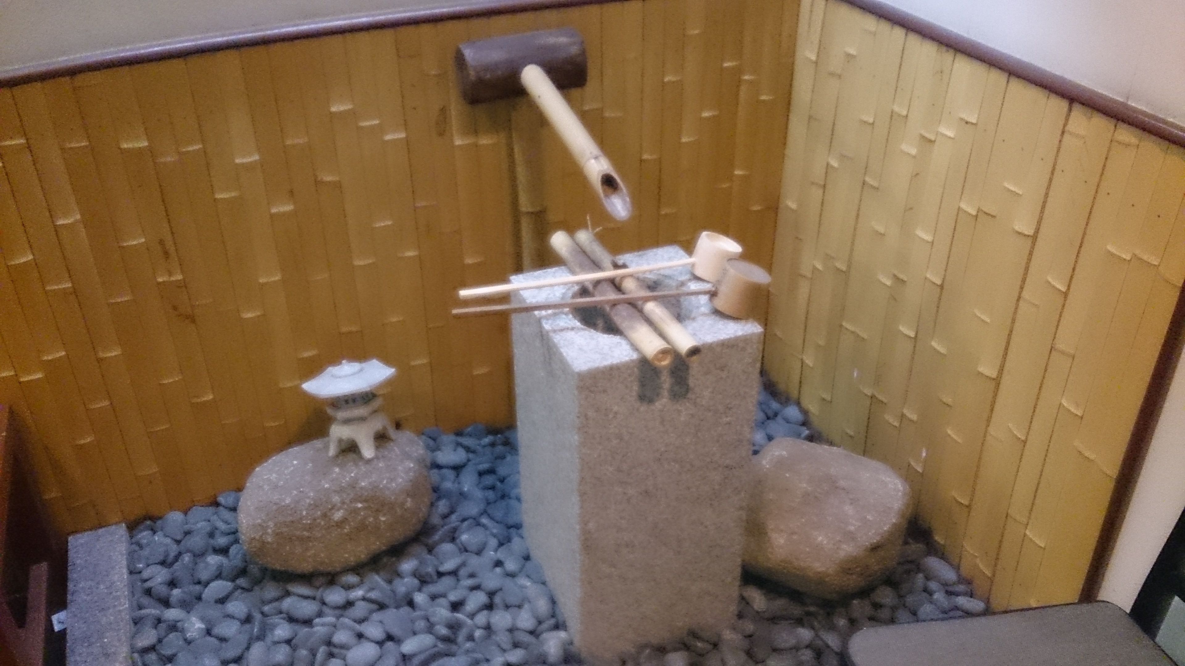 Un pequeño jardín interior con una fuente de piedra, una estructura de bambú y guijarros.