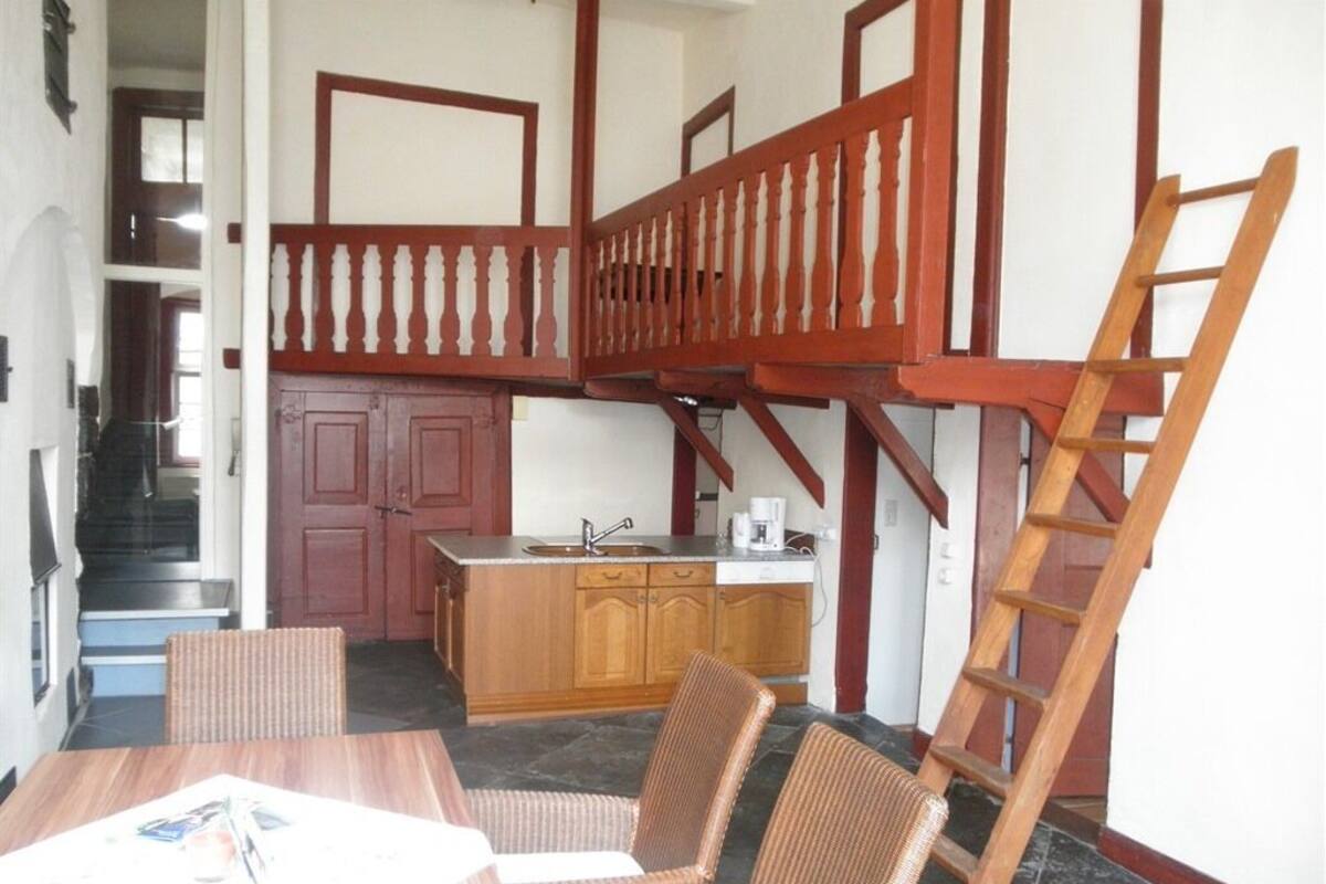 A spacious kitchen with a wooden staircase, a dining area with wicker chairs, and a kitchen counter with a sink.