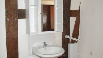 Casa de banho com lavatório branco, espelho e vigas de madeira.