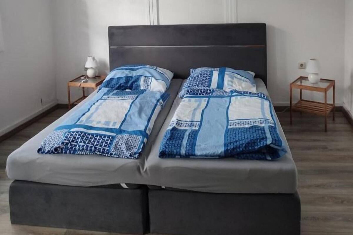 A bedroom with a bed, two bedside tables, and a hanging light fixture.