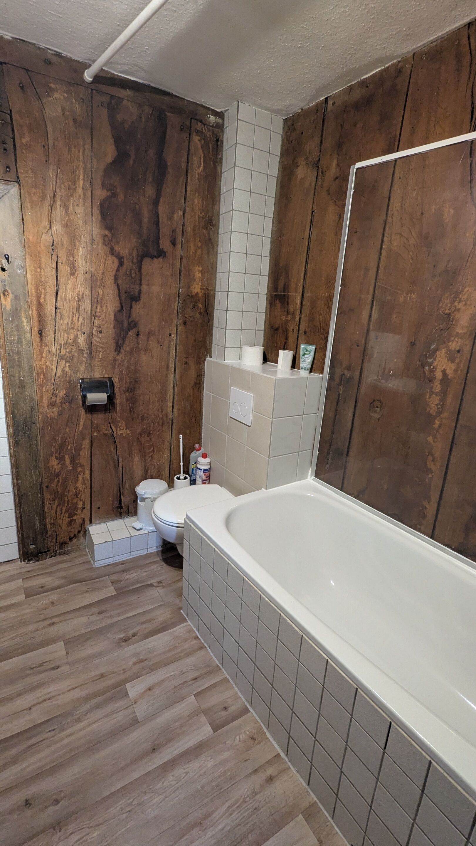 A bathroom with a wooden wall, a bathtub, a toilet, and a mirror.