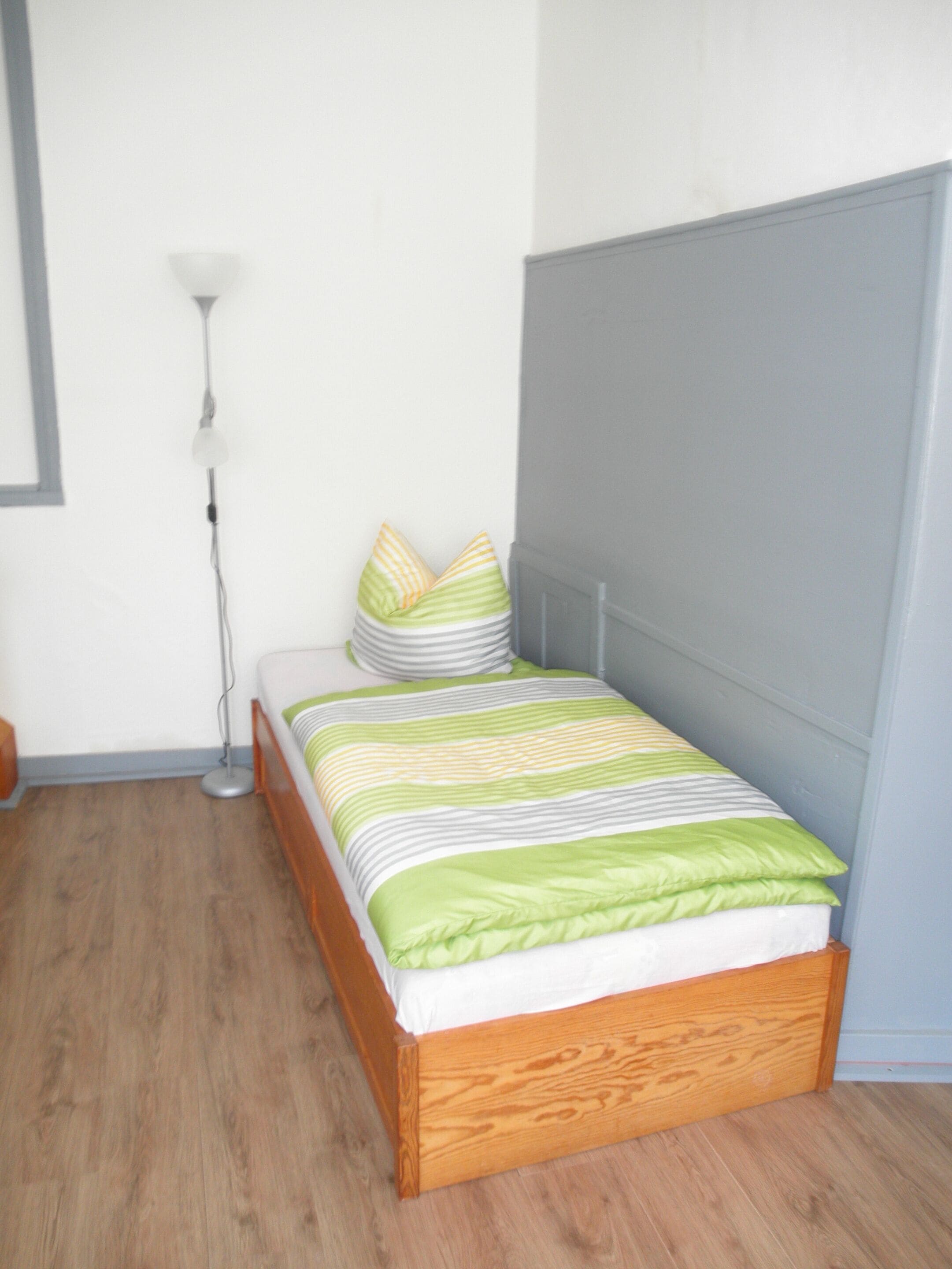 Una cama bien hecha con ropa de cama a rayas, una lámpara de noche y un suelo de madera.