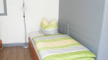 Una cama bien hecha con ropa de cama a rayas, una lámpara de noche y un suelo de madera.