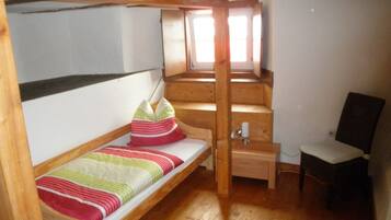 A small, cozy room with a bunk bed, a desk, and a chair.