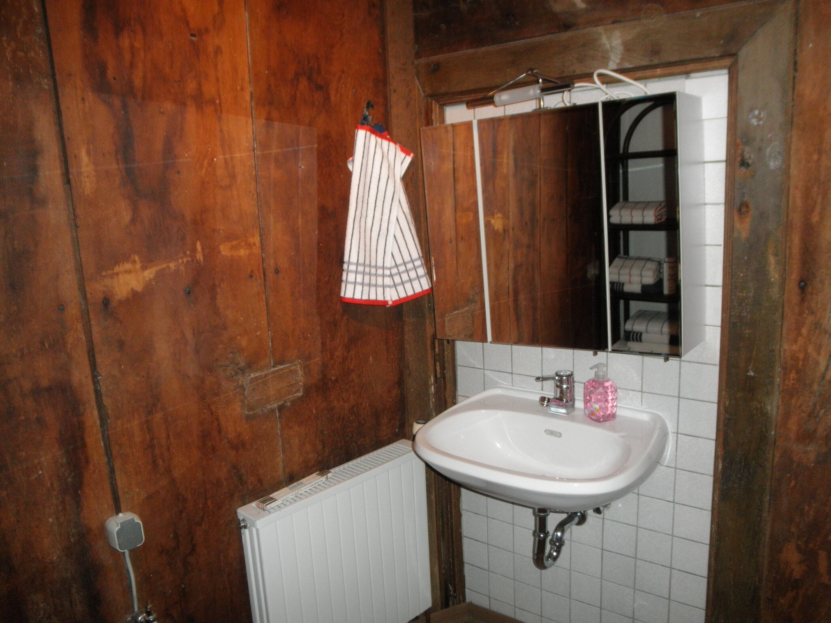 Une salle de bain avec un mur en bois, un lavabo blanc, un miroir et une serviette suspendue à un porte-serviettes.