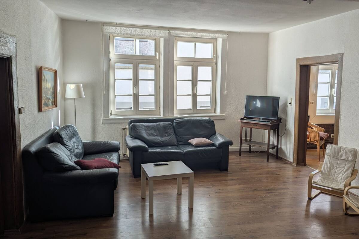 A living room with a sofa, a small table, a TV on a stand, and a chair.