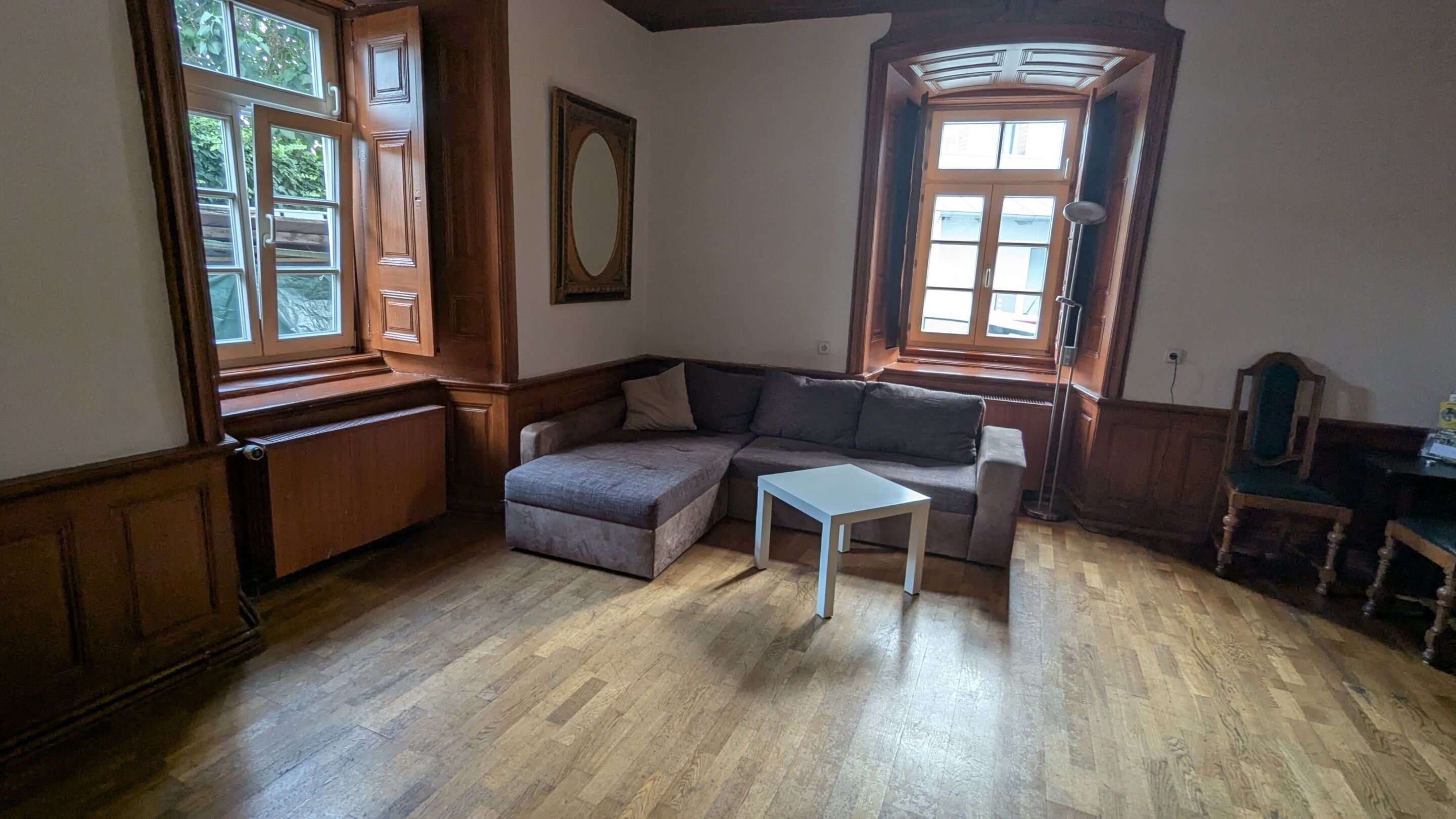 A room with a wooden floor, a sofa, a small table, and a chair.