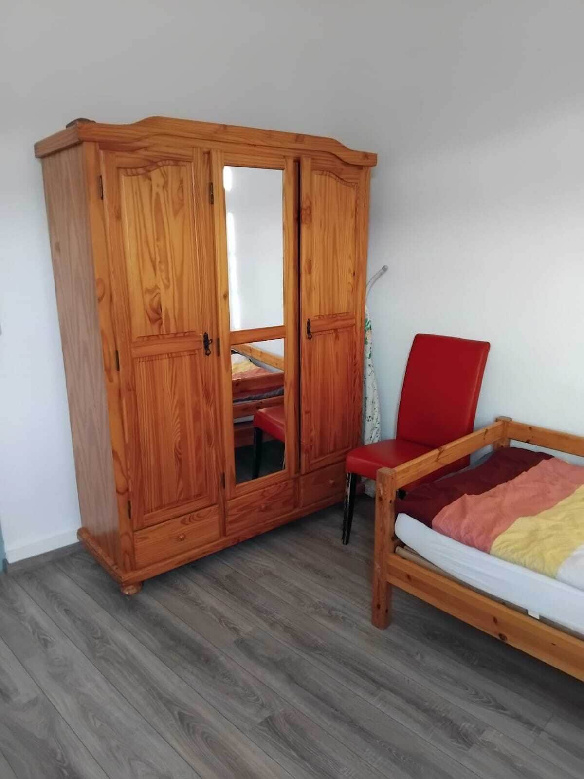 A room with a wooden wardrobe, a red chair, and a bed with a colorful blanket.