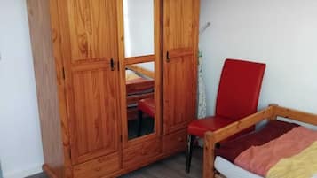 A room with a wooden wardrobe, a red chair, and a bed with a colorful blanket.