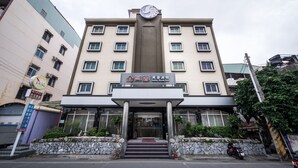 Un hotel de varios pisos con una entrada central, un reloj sobre la entrada y un letrero con texto.