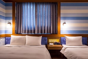 Habitación de hotel con dos camas, cabecero de madera, mesita de noche con teléfono y lámpara, y ventana con cortinas.
