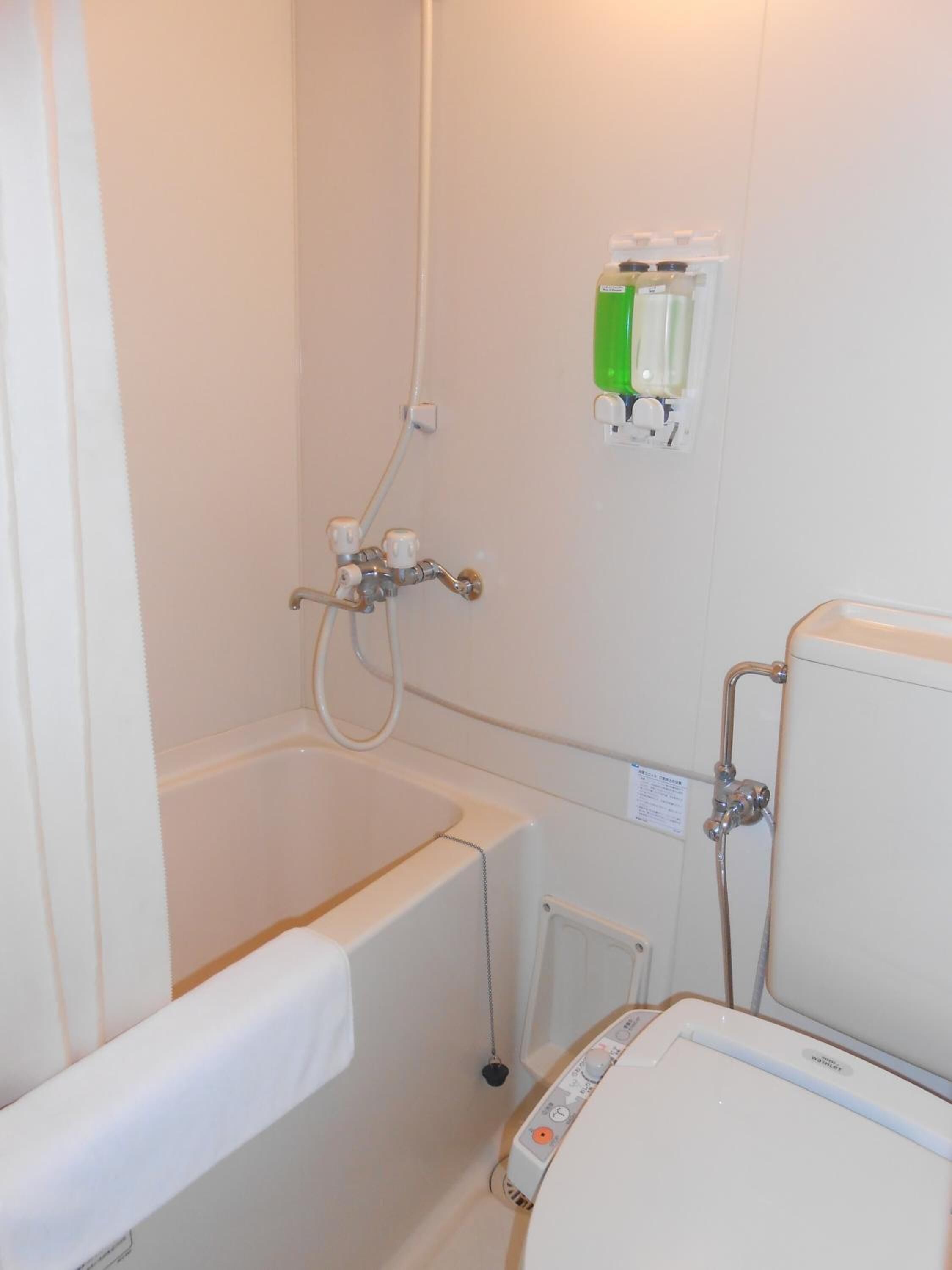 Un baño con bañera, ducha e inodoro. Hay un panel de control en la pared y una botella verde en la estantería.