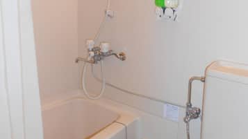 Un baño con bañera, ducha e inodoro. Hay un panel de control en la pared y una botella verde en la estantería.