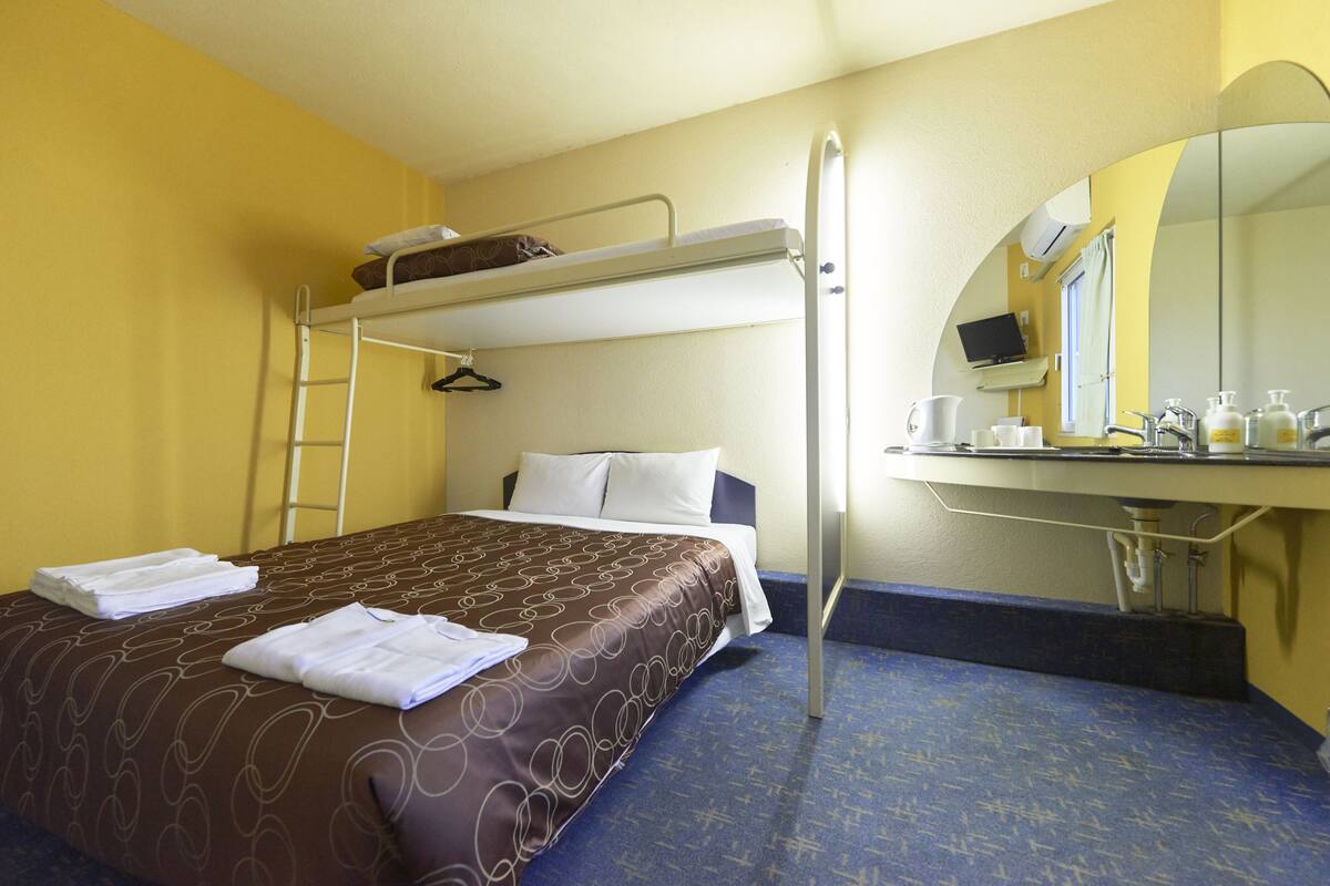 A hotel room with a bunk bed, a desk with a mirror, and a bathroom with a shower curtain.