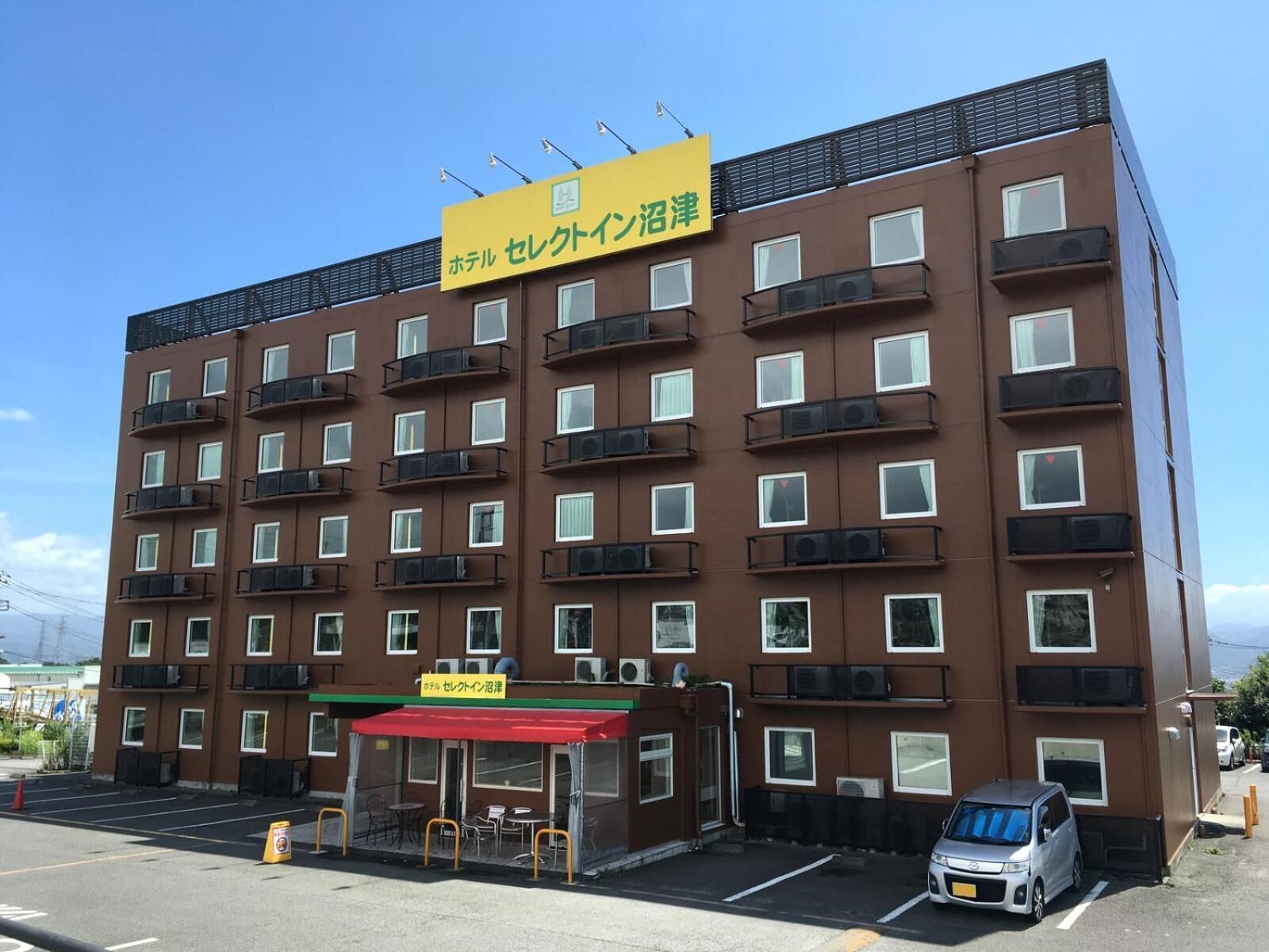 Un hotel de varios pisos con fachada marrón, múltiples balcones y un toldo rojo sobre la entrada.