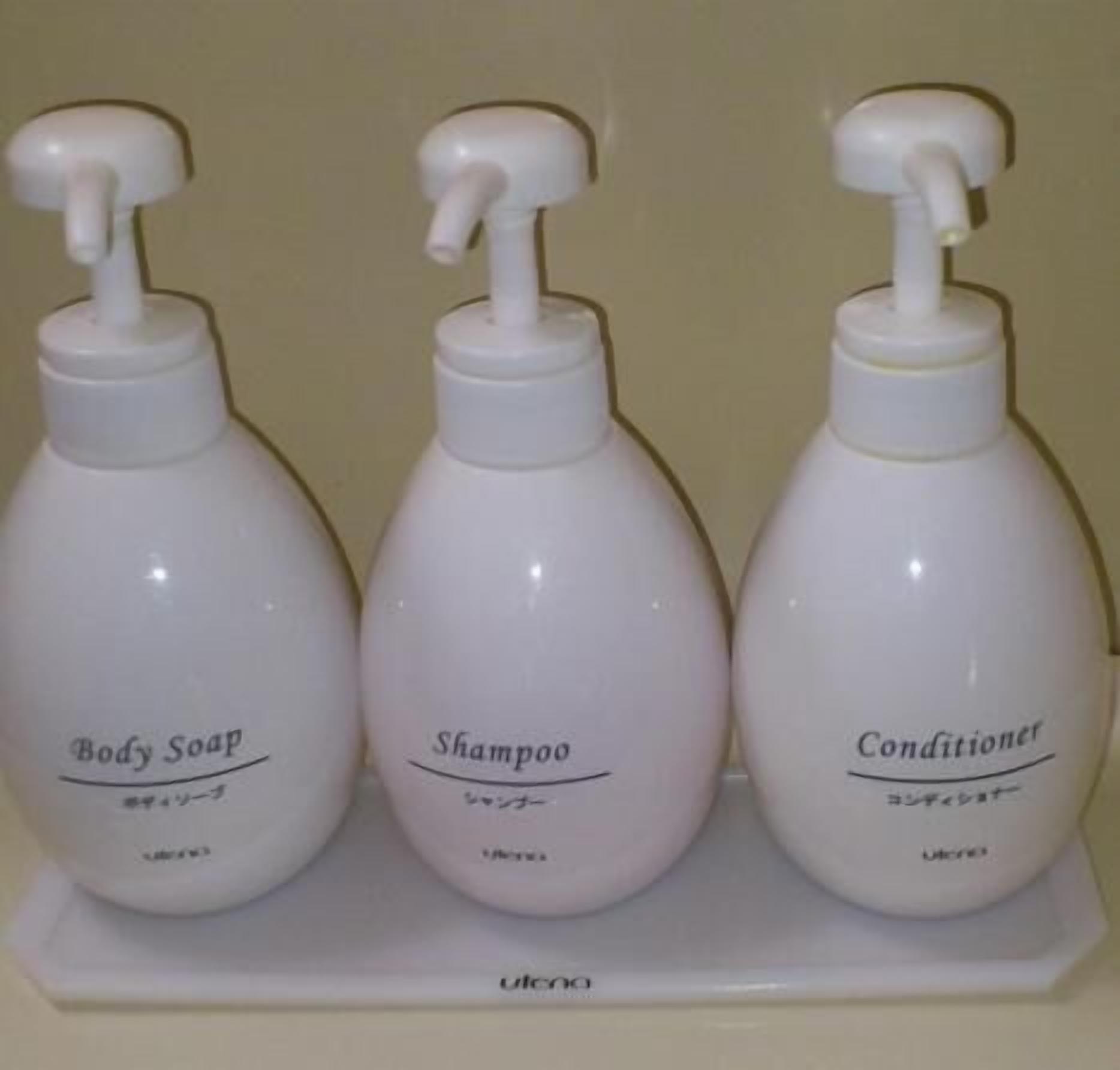 Three white bottles labeled 'Body Soap,' 'Shampoo,' and 'Conditioner' on a white shelf.
