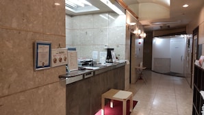 A hotel reception area with a marble counter, framed certificates, a small table, and a restroom in the background. - Hotel Select Inn Nagoya Iwakura Ekimae (Iwakura)