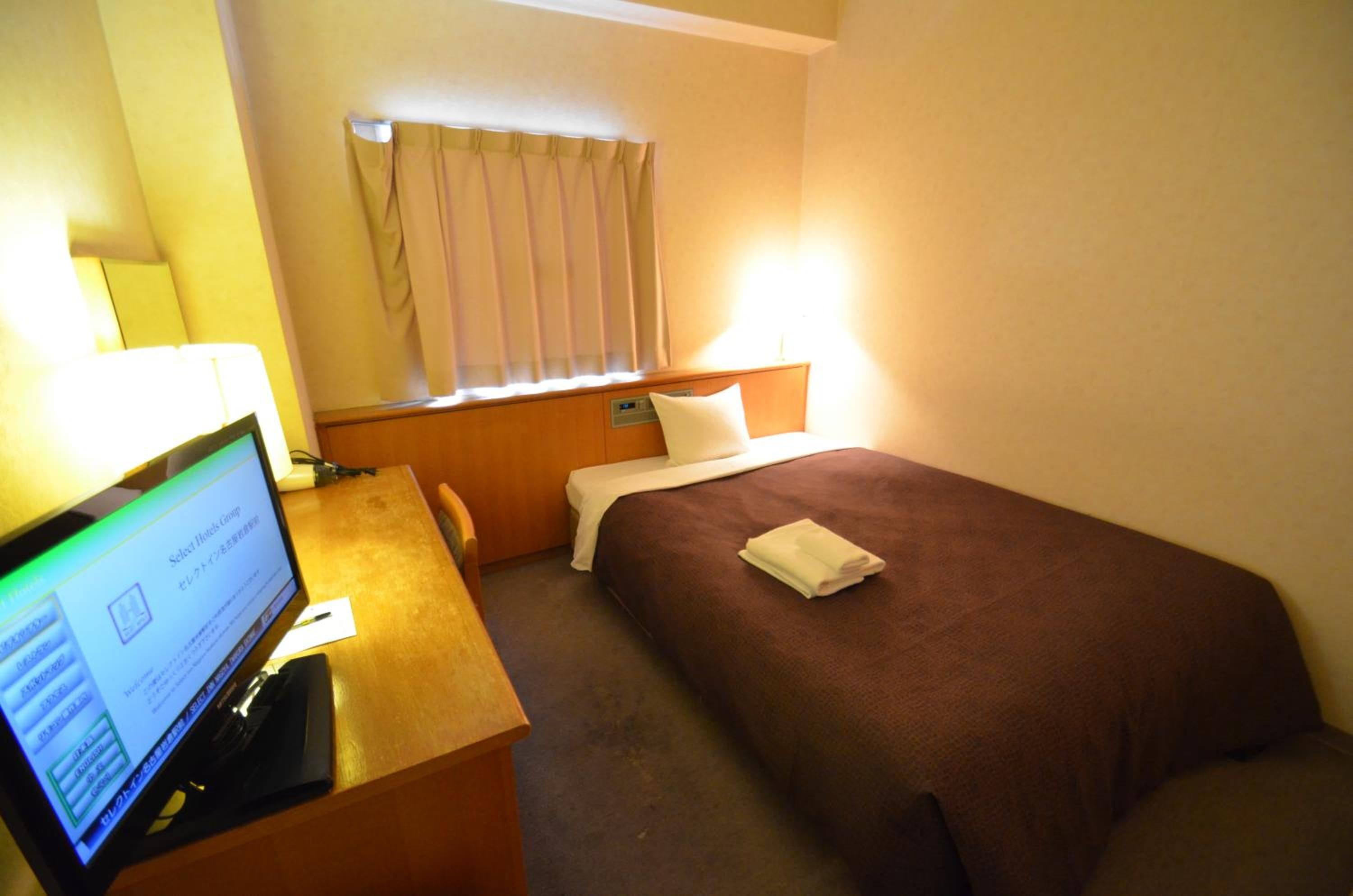 A hotel room with a bed, a desk with a computer, and a window with curtains.