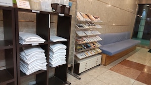 A reception area with a reception desk, a seating area with a blue sofa, and shelves with folded towels and magazines. - Hotel Select Inn Nagoya Iwakura Ekimae (Iwakura)