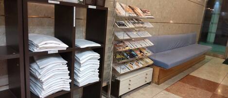 Zona de recepción con mostrador, área de descanso con sofá azul y estantes con toallas dobladas y revistas.