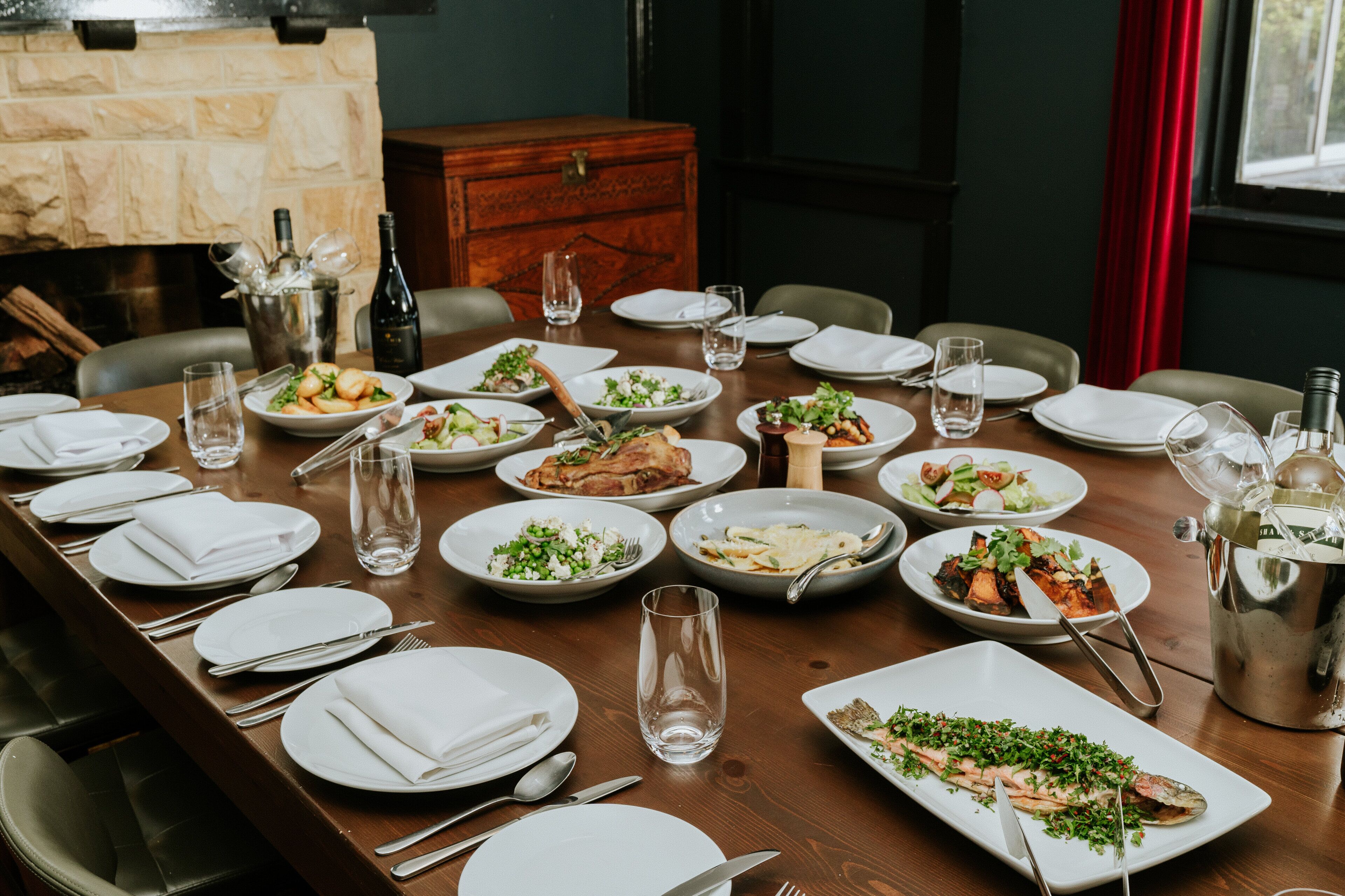 Una mesa de comedor servida con varios platos de comida, vasos y cubiertos.