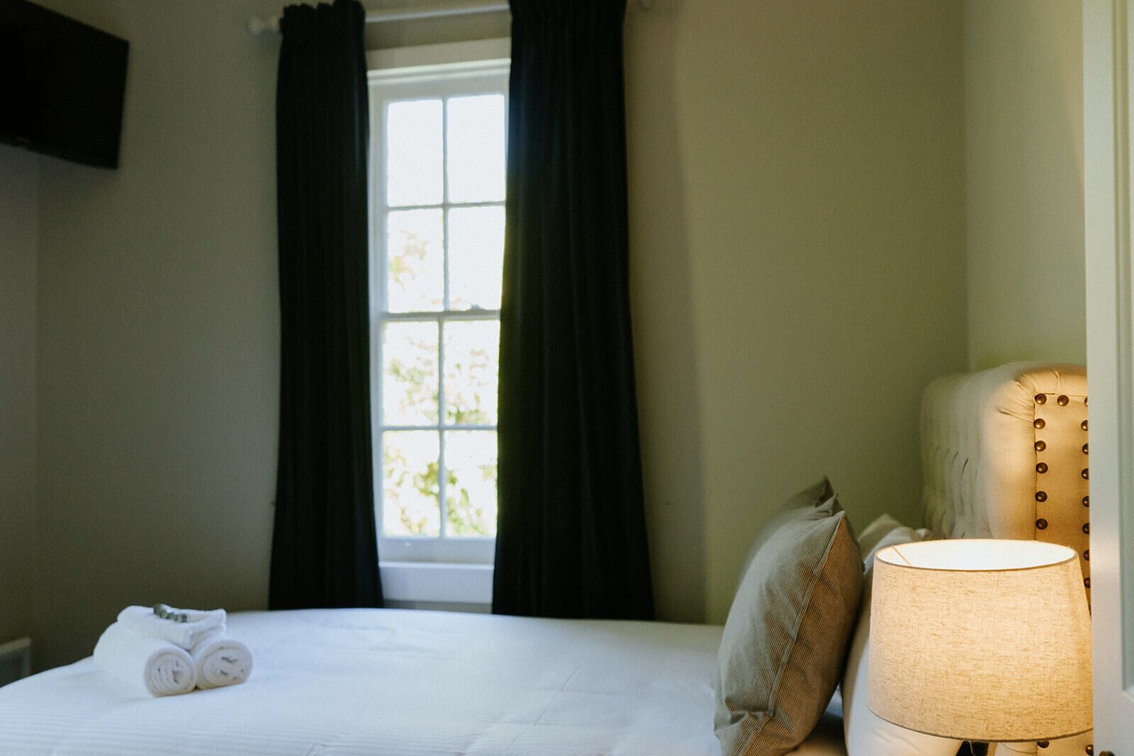 A hotel room with a bed, a lamp, and a window with curtains.