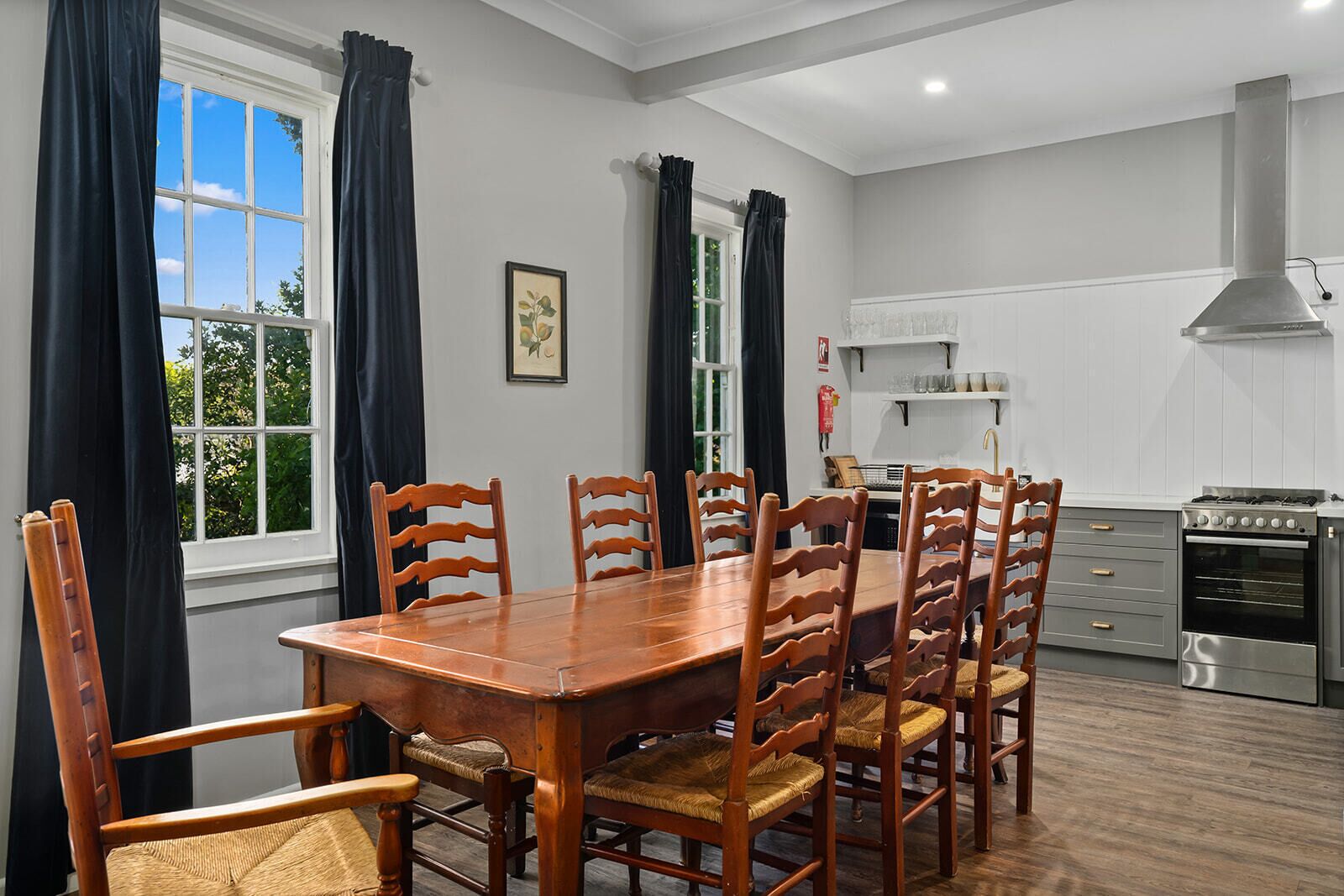 A dining area with a wooden table and chairs, a kitchen with modern appliances, and large windows with curtains.