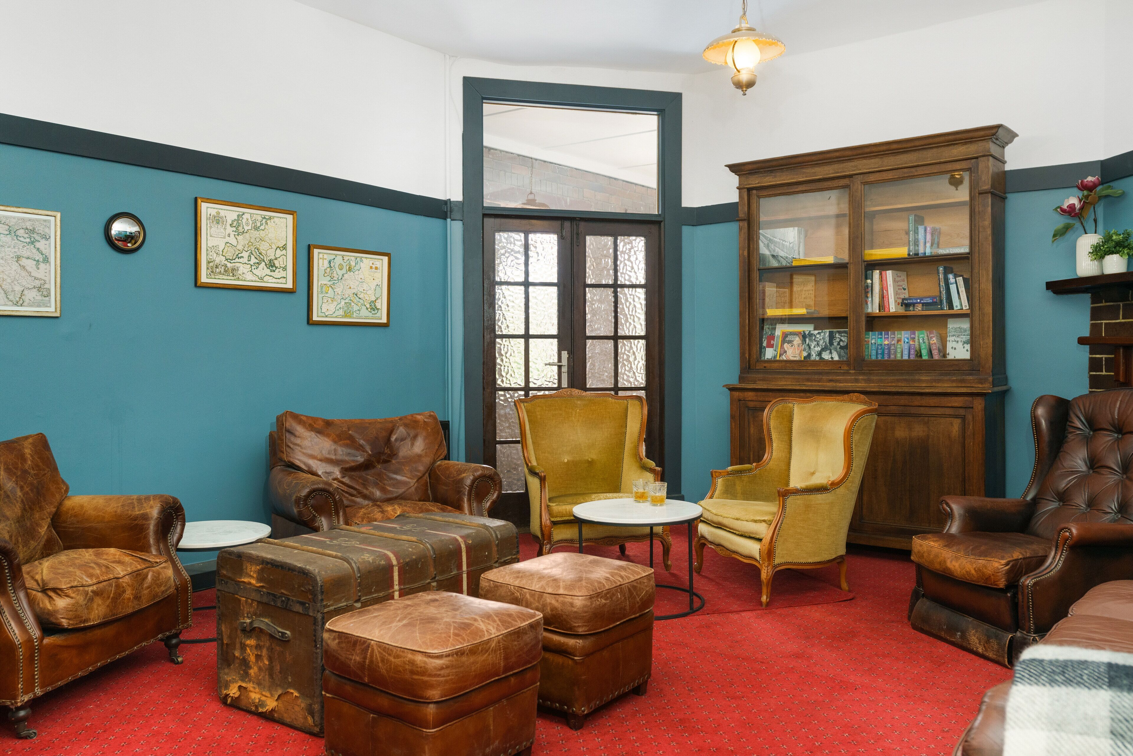 Una habitación con paredes azules, una estantería de madera, sillones de cuero y una alfombra roja.