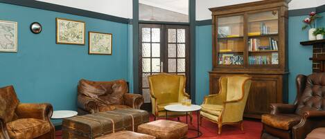 Una habitación con paredes azules, una estantería de madera, sillones de cuero y una alfombra roja.