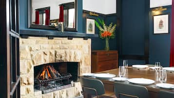 Un comedor con chimenea de piedra, una mesa de madera dispuesta para cuatro personas y un jarrón con flores.