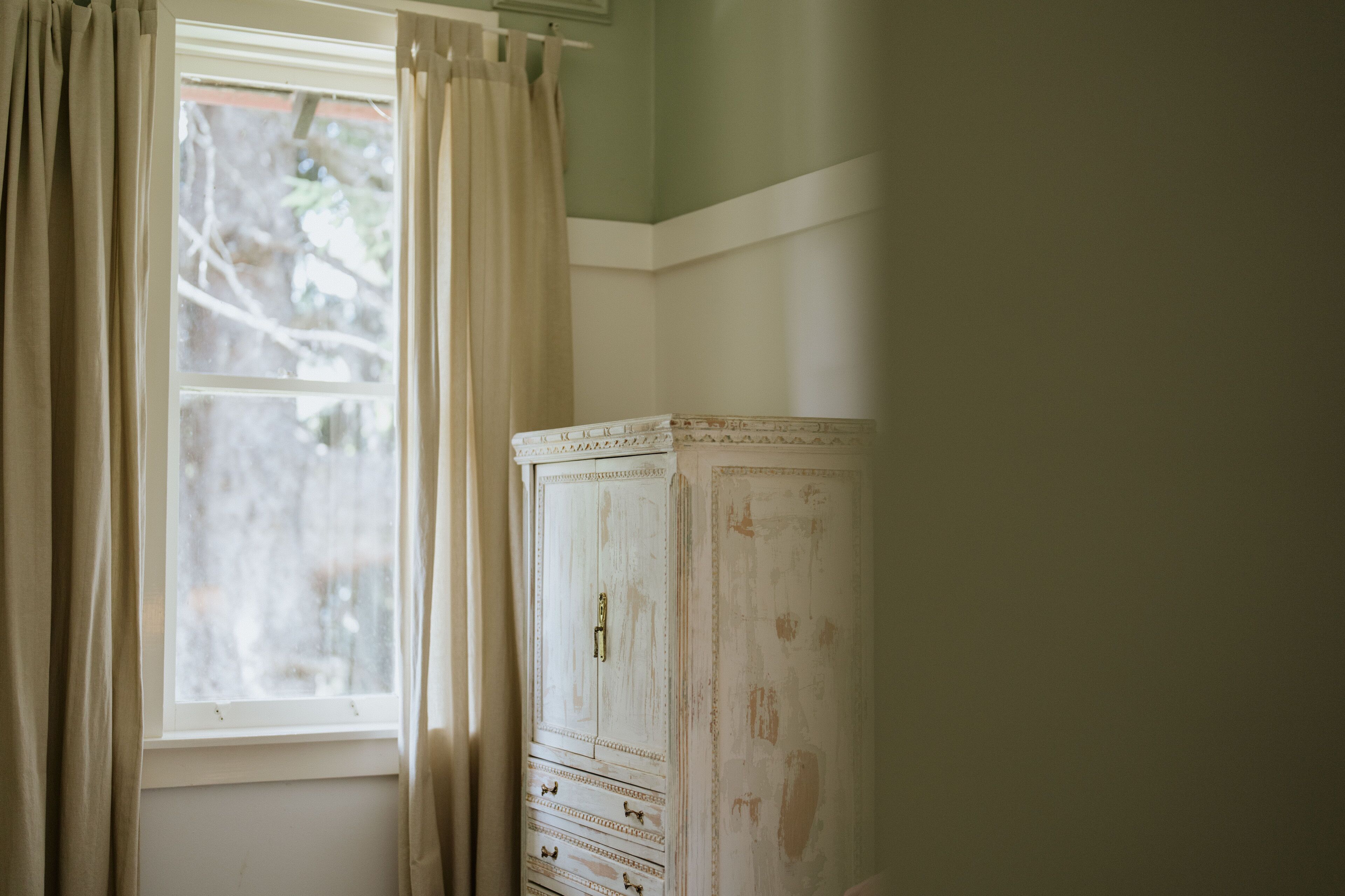 A room with a window, a white cabinet, and beige curtains.