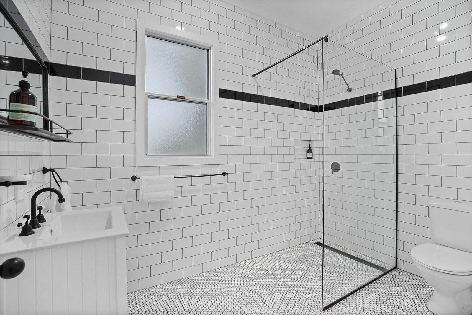 A modern bathroom with white subway tiles, a glass shower enclosure, a white sink with a black faucet, and a toilet.
