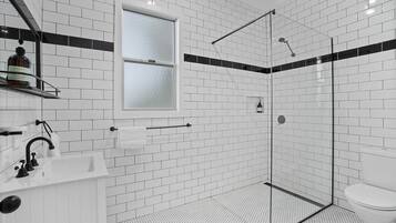 A modern bathroom with white subway tiles, a glass shower enclosure, a white sink with a black faucet, and a toilet.