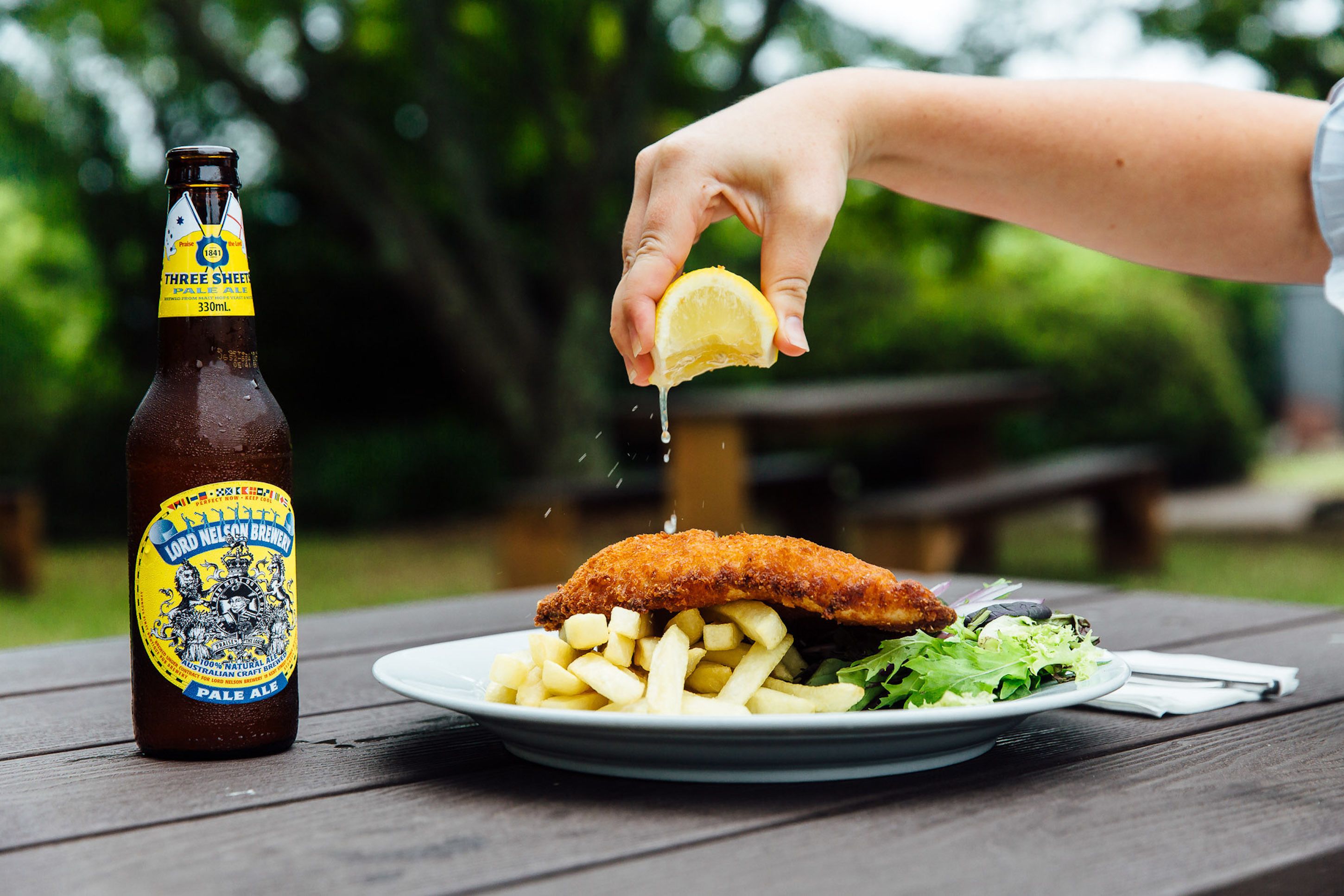 Una botella de cerveza y un plato con pescado y papas fritas sobre una mesa de madera.