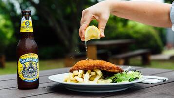 Una botella de cerveza y un plato con pescado y papas fritas sobre una mesa de madera.