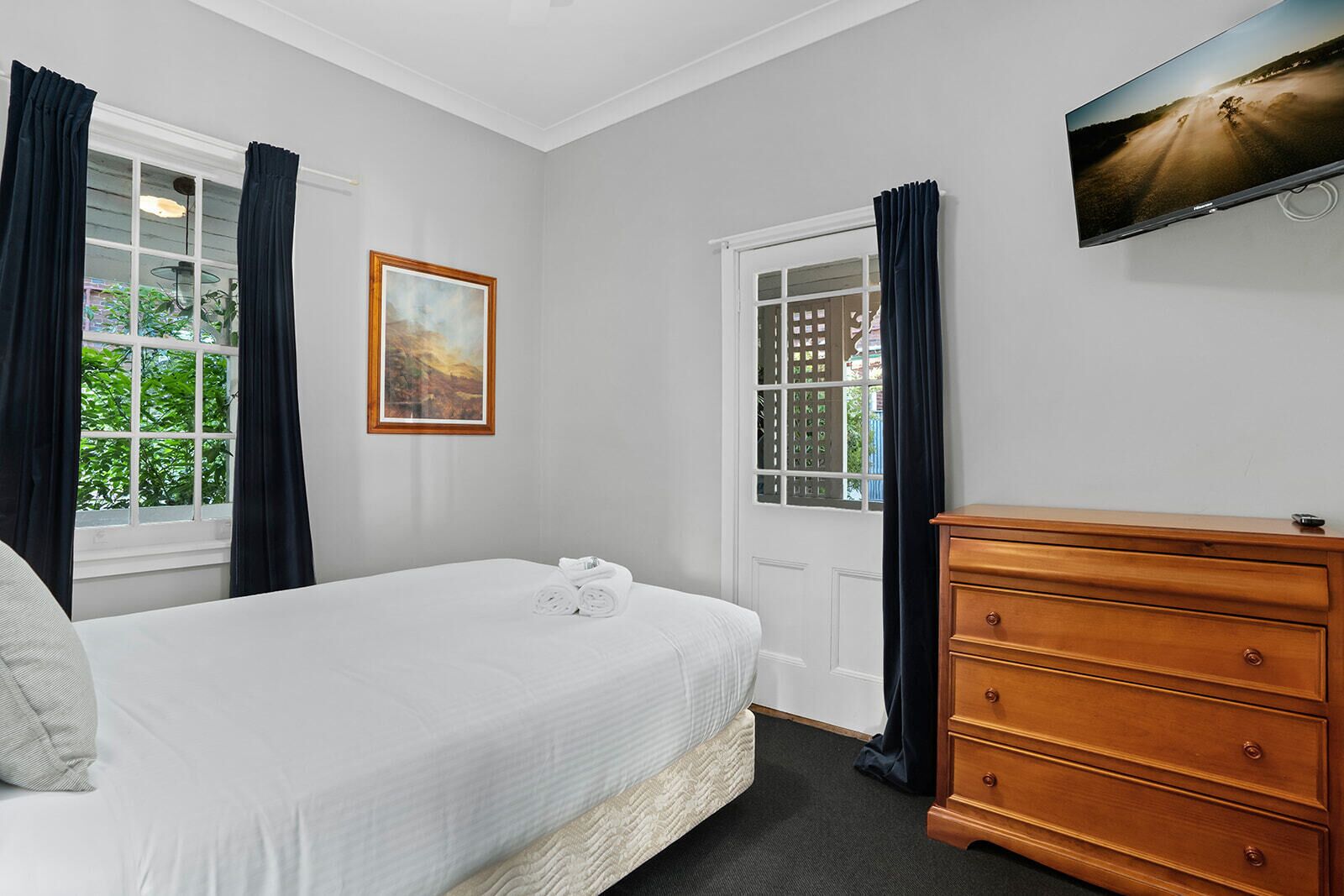 Un dormitorio con cama, cómoda, cuadro y televisor en la pared.