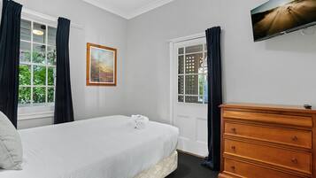 Un dormitorio con cama, cómoda, cuadro y televisor en la pared.
