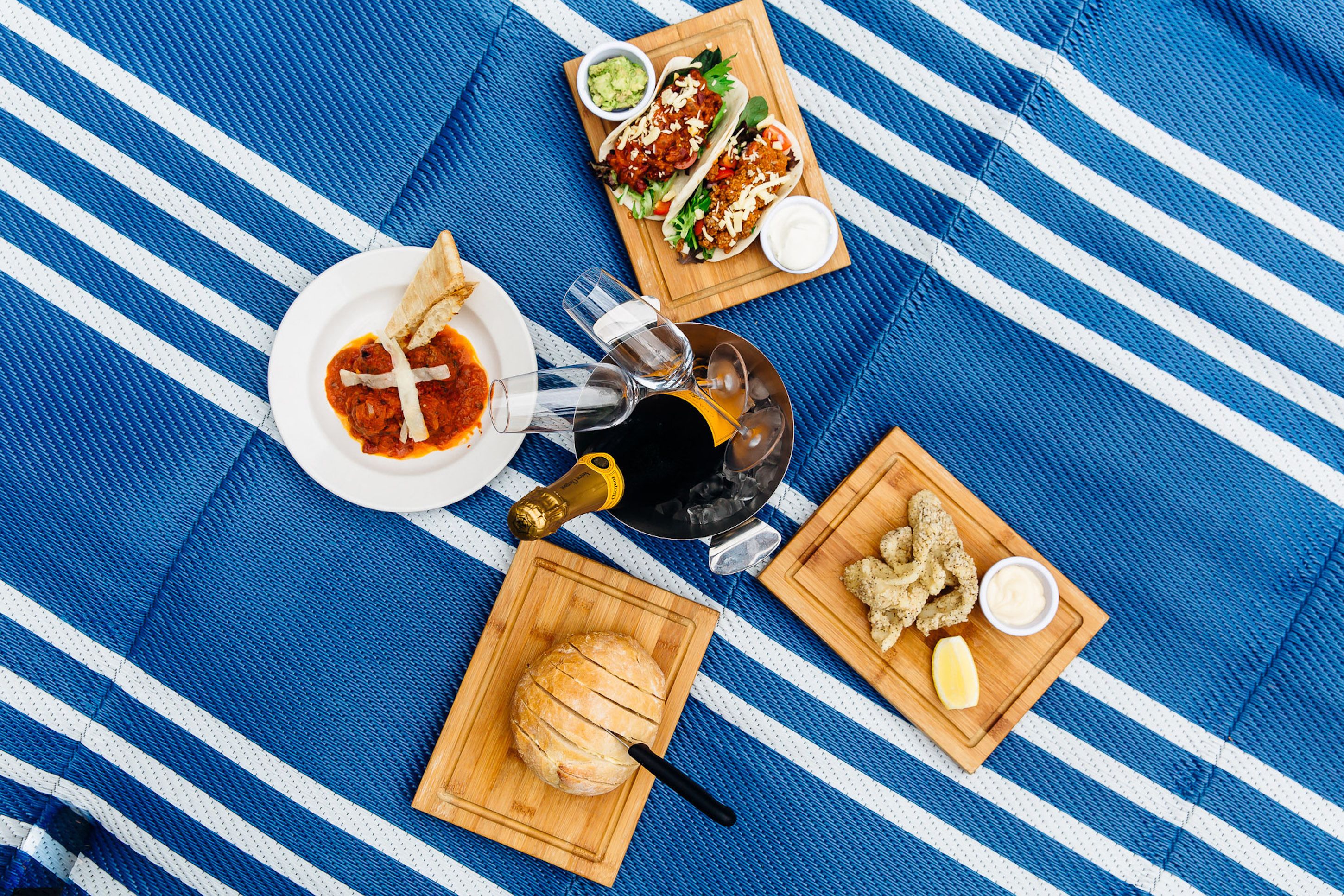 A meal setup with tacos, bread, and fried items on a blue-striped tablecloth.