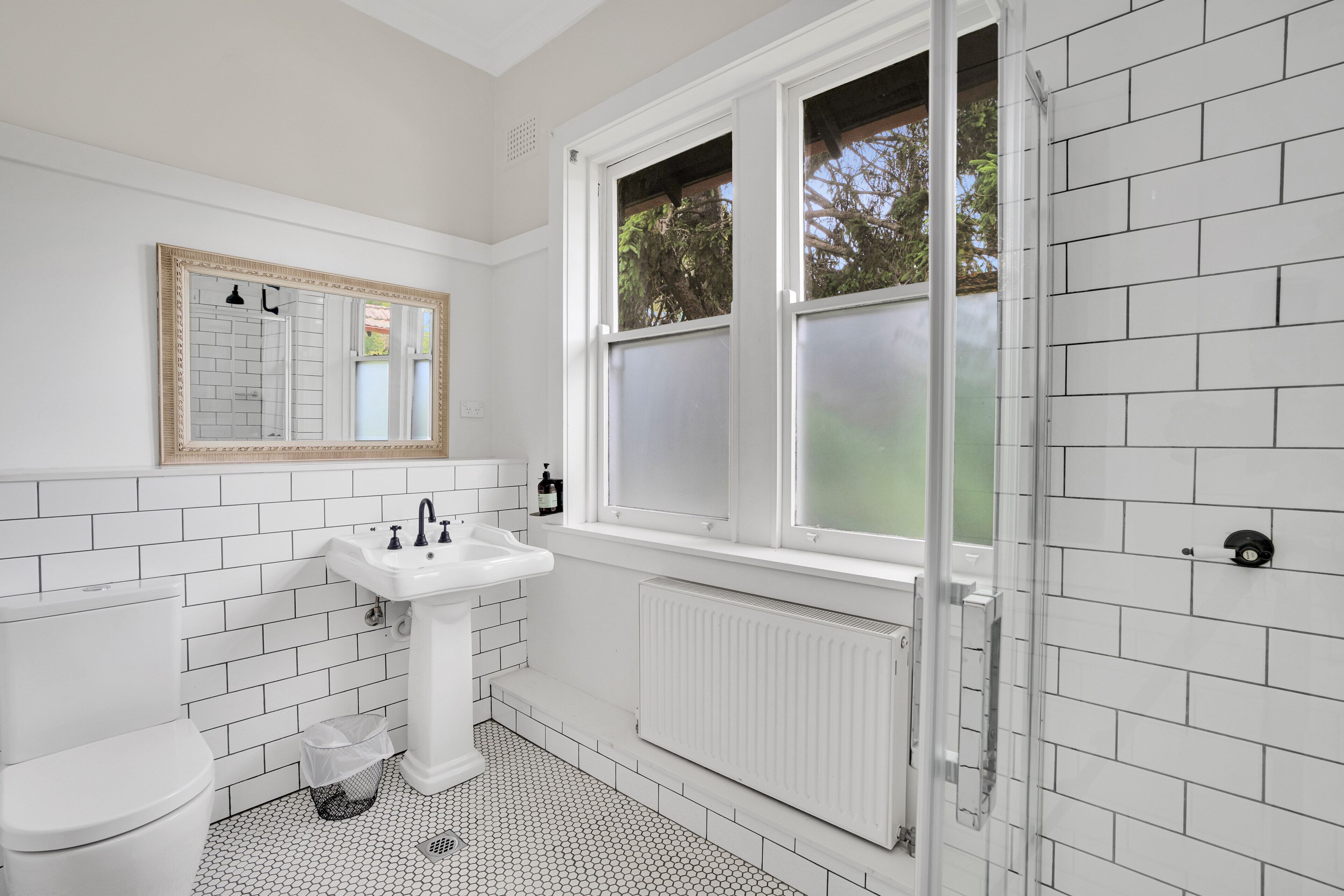 A bathroom with white tiled walls, a white sink, a toilet, and a window with frosted glass.