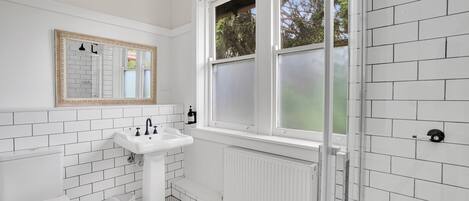 A bathroom with white tiled walls, a white sink, a toilet, and a window with frosted glass.