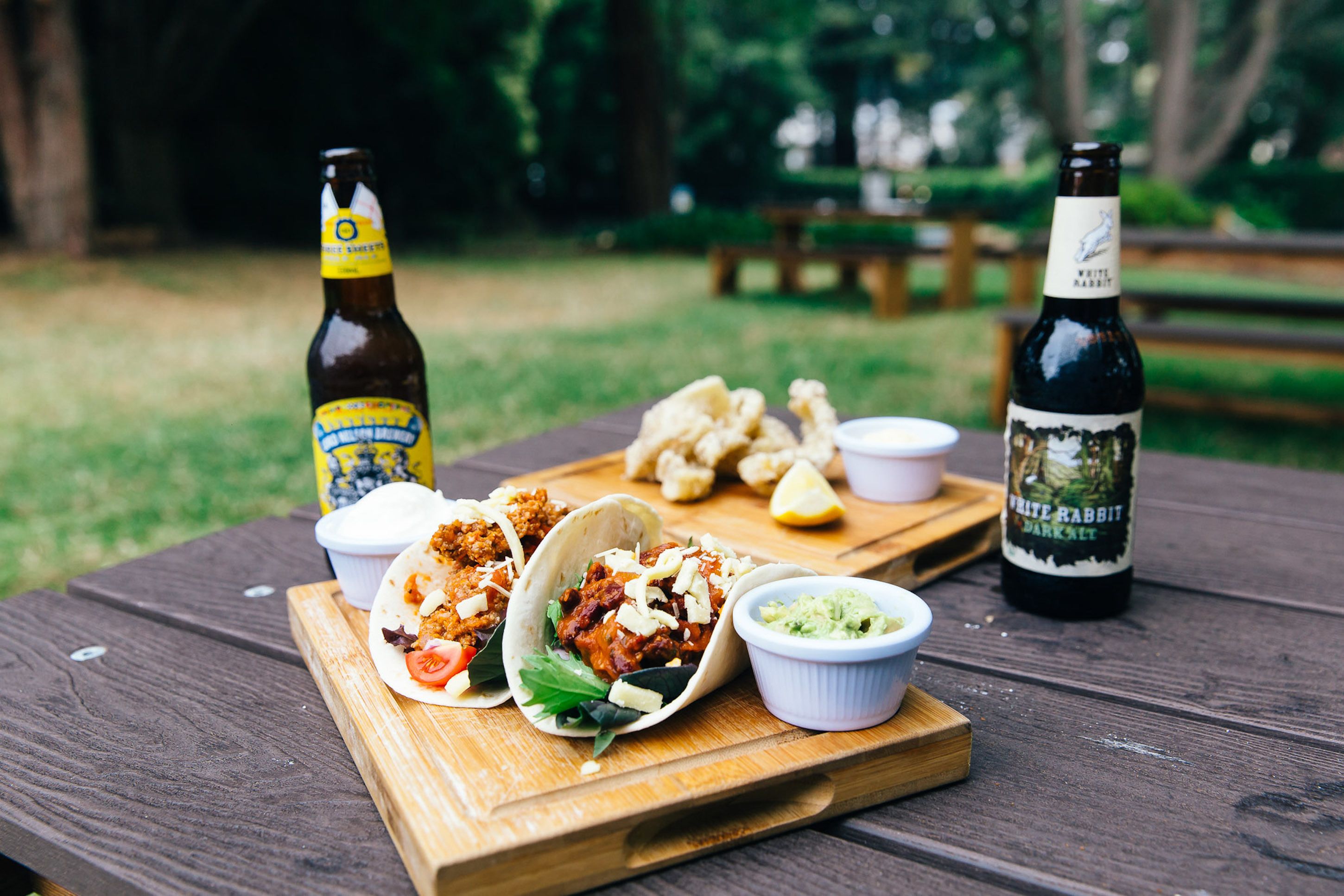 Una mesa de picnic con comida, incluyendo tacos y guacamole, y dos botellas de cerveza.