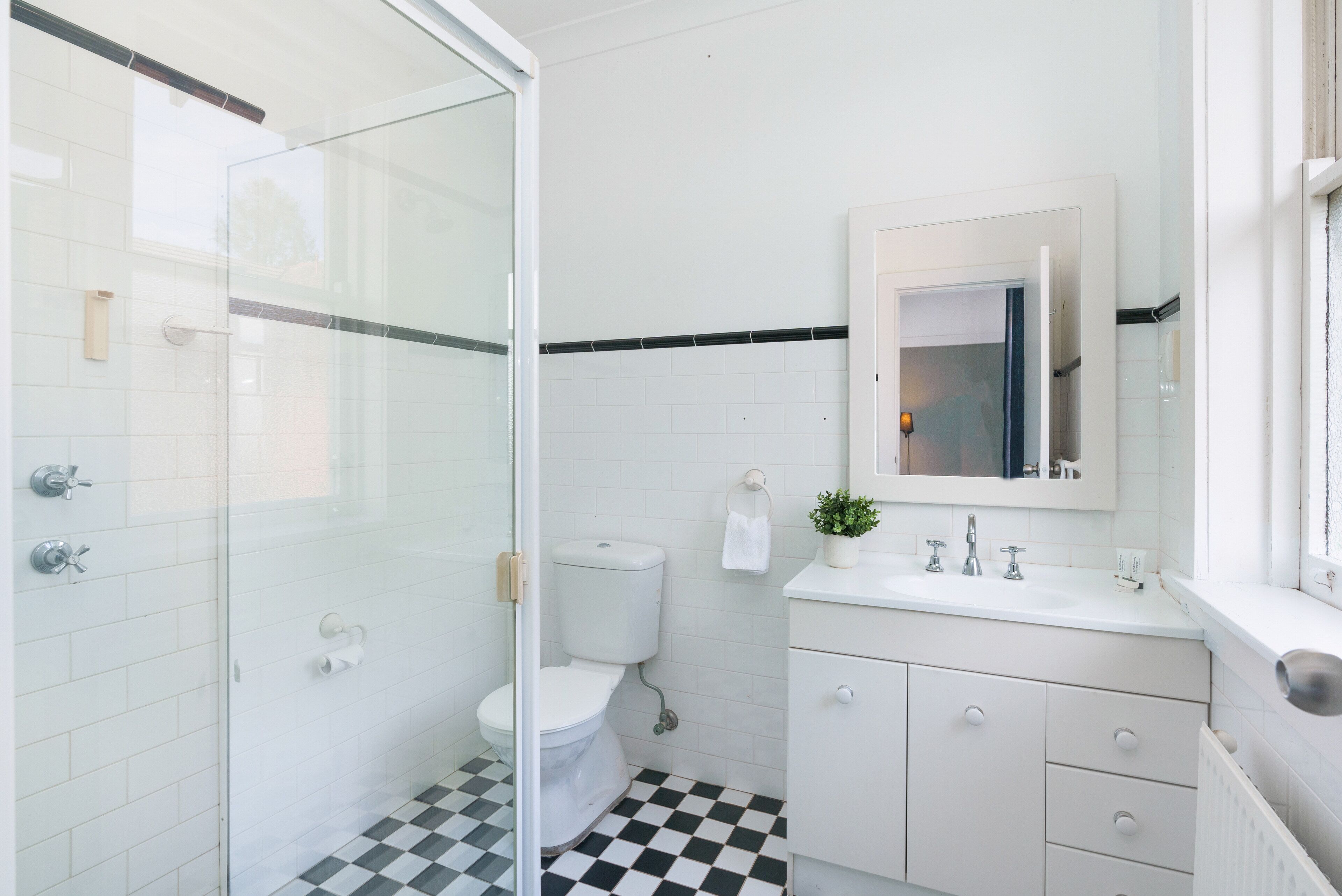 Un baño con cabina de ducha de vidrio, inodoro, lavamanos con espejo y suelo de cuadros.