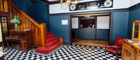 Eine Hotelhalle mit Schachbrettmuster-Boden, einer imposanten Treppe, einem Chandelier und einer Rezeption.