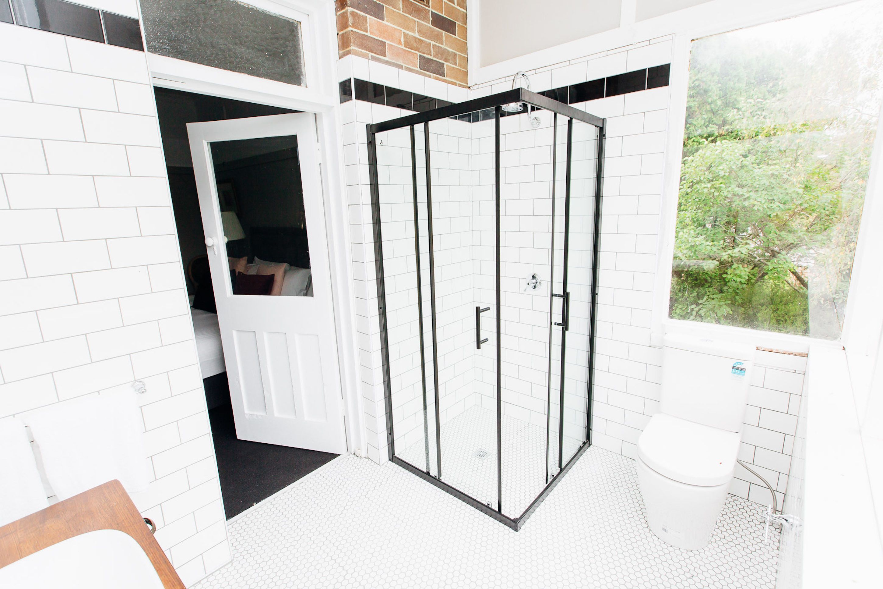 A bathroom with a glass shower enclosure, a white toilet, and a window with a view of greenery.