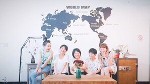 A group of people seated at a table with a world map in the background. - OC Hostel (Tainan)