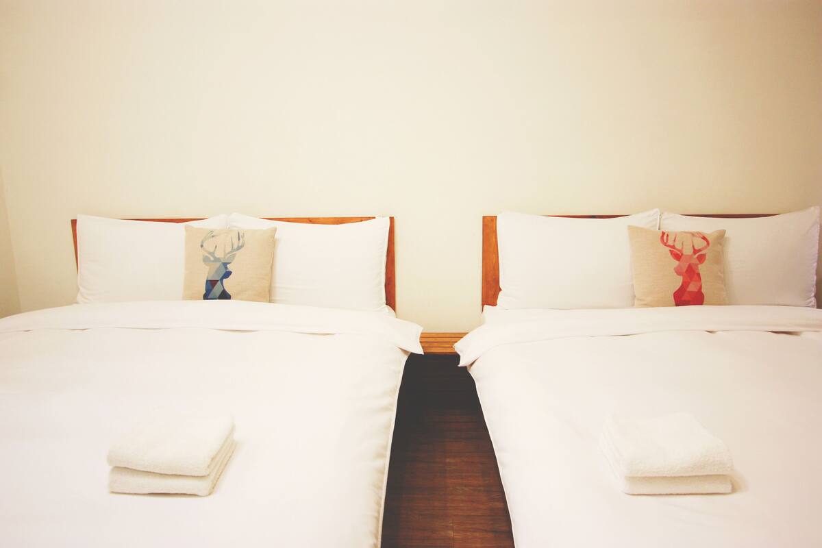 A double bed with white linens and two pillows, one with a deer design.