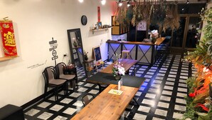 A restaurant with a checkered floor, wooden tables, and chairs. There are decorative plants and a clock on the wall. - OC Hostel (Tainan)