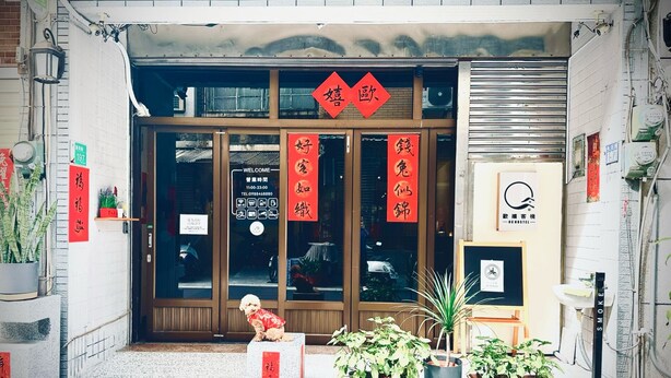 A storefront with large glass doors, red banners with Chinese characters, and a small dog sitting outside. - OC Hostel (Tainan)