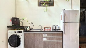 A compact kitchen with a washing machine, a refrigerator, a sink with a faucet, and a countertop with various items. - OC Hostel (Tainan)