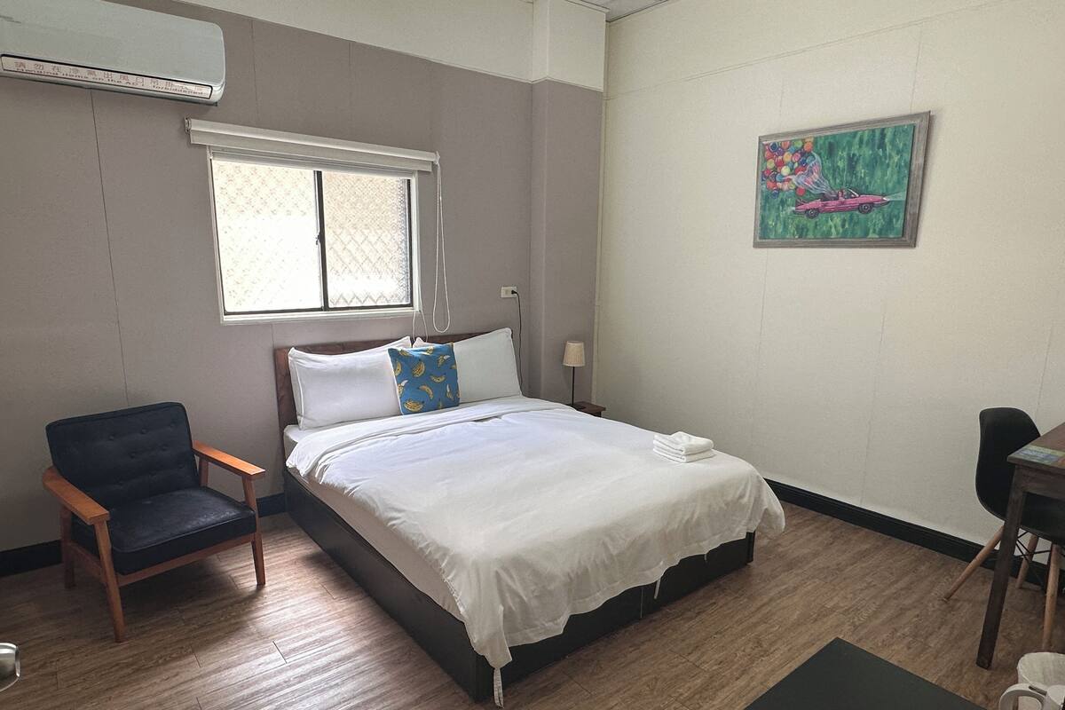 A hotel room with a bed, a chair, a desk, and a window.